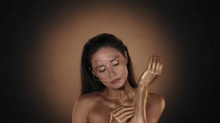 Téléchargez les photos : Portrait de femme attirante. Gros plan d'un mannequin féminin avec des larmes d'or sur les joues, enlevant la peinture dorée sèche de la peau. Concept de publicité. - en image libre de droit