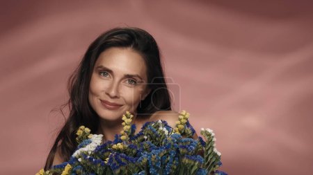 Téléchargez les photos : Une femme avec un bouquet de fleurs sauvages fraîches. Séminude femme dans le studio sur un fond rose gros plan. Le concept de beauté, cosmétologie, soins, spa, santé des femmes - en image libre de droit