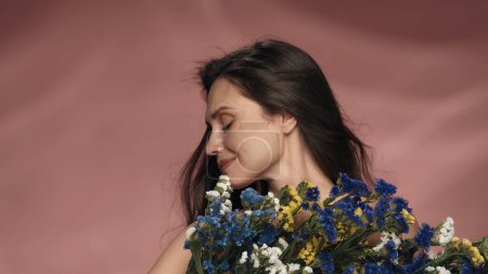Téléchargez les photos : Profil portrait d'une femme avec un bouquet de fleurs sauvages fraîches. Séminude femme dans le studio sur un fond rose gros plan. Le concept de beauté, cosmétologie, soins, spa, santé des femmes - en image libre de droit