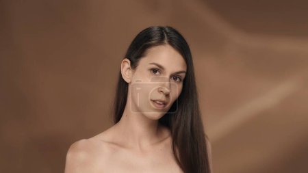 Foto de Retrato de una joven mujer de cabello largo en el estudio sobre un fondo marrón. El concepto de belleza, cosmetología, cuidado y salud de la mujer - Imagen libre de derechos