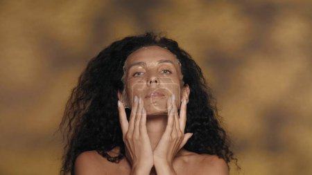 Téléchargez les photos : Une femme lisse un hydrogel cosmétique, masque de silicone sur son visage. Portrait d'une séminude en studio sur fond jaune avec des reflets. Le concept de beauté, de cosmétologie, de soins - en image libre de droit