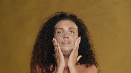 Photo for Woman in white cosmetic sheet mask on her face. Portrait of a seminude woman in the studio on a yellow background. The concept of beauty, cosmetology, care - Royalty Free Image