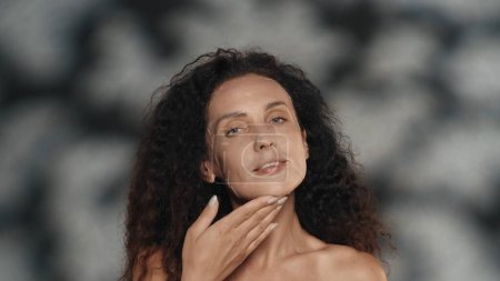 Téléchargez les photos : Femme en drap cosmétique blanc masque sur son visage. Portrait d'une femme séminude en studio sur fond noir avec des reflets. Le concept de beauté, de cosmétologie, de soins - en image libre de droit