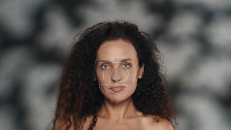 Téléchargez les photos : Femme en drap cosmétique blanc masque sur son visage. Portrait d'une femme séminude en studio sur fond noir avec des reflets. Le concept de beauté, de cosmétologie, de soins - en image libre de droit