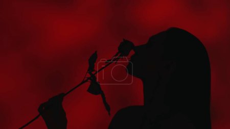 Foto de Vídeo de cerca del perfil lateral de una joven silueta de mujer sosteniendo una rosa roja en su mano y arrastrándola por su cara. Fondo rojo oscuro. Publicidad de ocio o producto. - Imagen libre de derechos