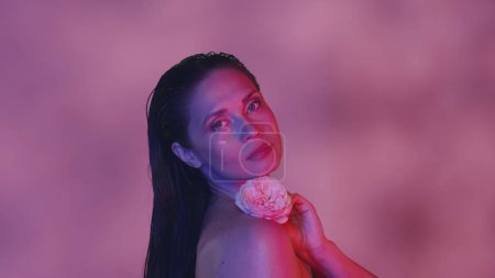 Photo for Close up shot of an attractive young seminaked woman. She is holding a pink rose flower in her hand, looking at the camera with tenderness. Pink color scheme. Creative content. - Royalty Free Image