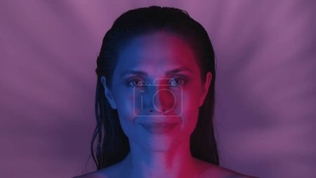 Photo for Close up shot of a young womans face. She is confidently looking at the camera in joyful and alluring manner, neon pink and blue color scheme. Leisure or product advertisement. - Royalty Free Image