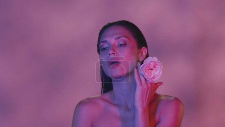 Téléchargez les photos : Gros plan d'une jolie jeune femme séminarisée. Elle regarde vers le côté et exhalant la fumée avec une fleur rose dans sa main, schéma de couleur rose. Contenu créatif. - en image libre de droit