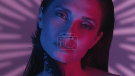Photo for Close up shot of a young womans face. She is looking at the camera, relaxed and meditative, in a neon pink and blue color scheme. Leisure or product advertisement. - Royalty Free Image