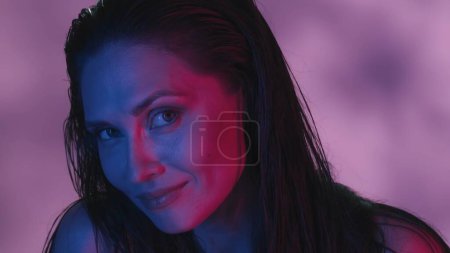 Photo for Close up shot of a young womans face. She is confidently looking at the camera and is flirtingly raising her eyebrow, neon pink and blue color scheme. Leisure or product advertisement. - Royalty Free Image