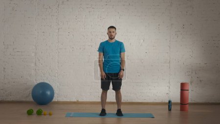 Photo for Sport indoors. Athletic man fitness coach doing exercises at the home studio for online classes. Man in sportswear doing a neck warm up. Healthcare and wellness concept. - Royalty Free Image