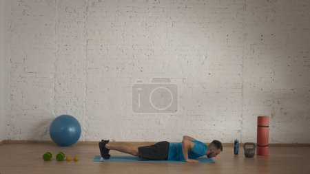 Athletic man fitness coach doing exercises at the home studio for online classes. Man in sportswear doing burpee . Healthcare concept.