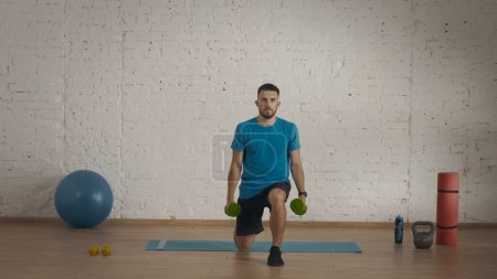Photo for Personal sport trainings at home. Athletic man fitness coach doing exercises at the home studio for online classes. Man in sportswear doing lunges exercise with kettlebell. - Royalty Free Image