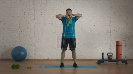 Photo for Athletic male fitness coach doing exercises at the home studio for online classes. Man in sportswear doing pulling to chest rubber band exercise. - Royalty Free Image