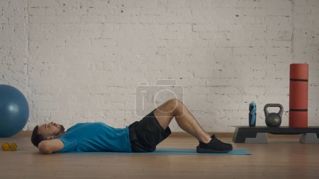 Foto de Entrenador de fitness masculino atlético haciendo ejercicios en el estudio en casa para clases en línea. Hombre en ropa deportiva haciendo ejercicios crujidos. - Imagen libre de derechos