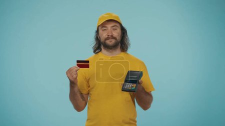 Photo for Portrait of a delivery man holding portable terminal and bank credit card. Online payments. Isolated on blue background. - Royalty Free Image