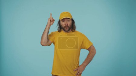 Photo for Courier service concept. Portrait of a delivery man, with focused face, thinking about an idea, pointing his finger. Isolated on blue background. - Royalty Free Image