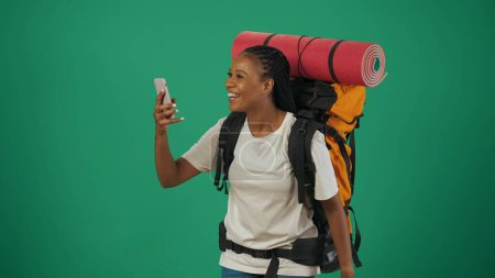 Téléchargez les photos : Une voyageuse enregistre des vidéos sur son smartphone. Portrait d'une touriste en tenue décontractée avec sac à dos. Voyager en temps libre concept. Isolé sur fond vert. - en image libre de droit