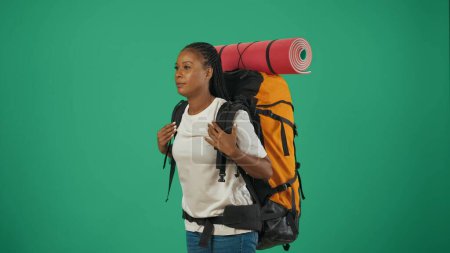 Téléchargez les photos : Une voyageuse fatiguée, triste. Portrait d'une touriste en tenue décontractée avec sac à dos. Voyager en temps libre concept. Isolé sur fond vert. - en image libre de droit