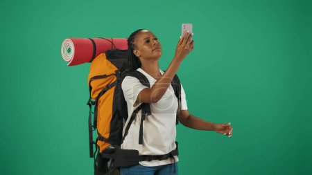Téléchargez les photos : Femme voyageur à la recherche de la connexion wifi réseau mobile. Portrait d'une touriste en tenue décontractée avec sac à dos. Voyager en temps libre concept. Isolé sur fond vert. - en image libre de droit