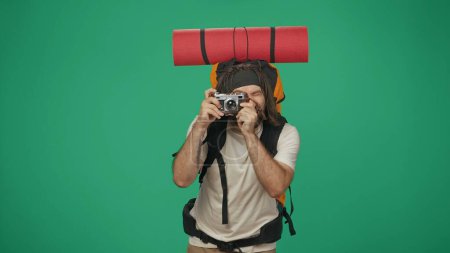 Téléchargez les photos : Voyageur tenant un vieil appareil photo, prenant des photos. Portrait d'un touriste masculin en vêtements décontractés avec sac à dos. Voyager en temps libre concept. Isolé sur fond vert. - en image libre de droit