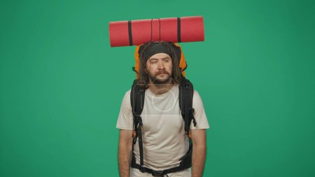 Photo for Man traveller looking tired of the trip. Portrait of a male tourist in casual clothes with backpack. Travelling in spare time concept. Isolated on green background. - Royalty Free Image