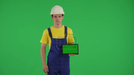 Photo for Medium green screen isolated chroma key shot of a young construction worker holding a laptop with advertising area, workspace mock up. Construction, repair advertisement. App, site. - Royalty Free Image