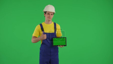 Photo for Medium green screen isolated chroma key shot of a young construction worker holding a laptop with advertising area, workspace mock up. Construction, repair advertisement. App, site. - Royalty Free Image