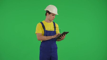 Téléchargez les photos : Ecran vert moyen, clef chromatique isolée d'un jeune ouvrier de la construction tenant une tablette et tapant, insérant des données. Construction, publicité de réparation. App, site. - en image libre de droit