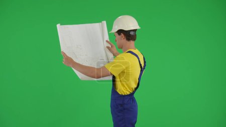 Photo for Medium green screen isolated chroma key shot of a young construction worker studying and comparing his plan to the surroundings. Construction, repair advertisement. Safety, reliability, confidence. - Royalty Free Image