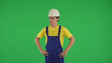 Téléchargez les photos : Ecran vert moyen isolé cliché chromatique d'un jeune ouvrier de la construction regardant autour, les mains sur les hanches. Construction, publicité de réparation. Sécurité, fiabilité. - en image libre de droit