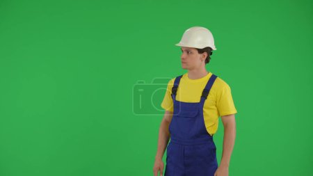 Photo for Medium green screen isolated chroma key shot of a young construction worker looking around, checking the surroundings. Construction, repair advertisement. Safety, reliability. - Royalty Free Image