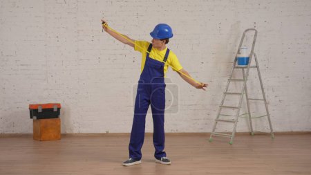 Photo for Full length shot of a young construction foreman standing in the room under renovation, unfolding the construction tape measure. Repairing, company advertisement. - Royalty Free Image