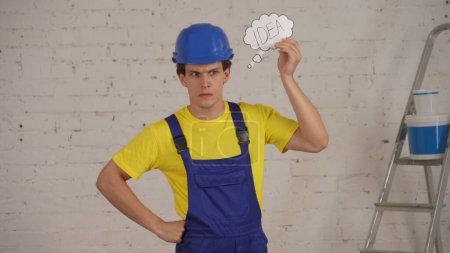 Photo for Medium shot of a young construction worker standing in the room under renovation, getting an idea, pensively looking away. Man is glad and happy. Construction, repair, company advertisement. - Royalty Free Image
