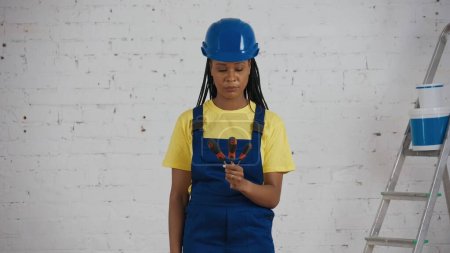 Photo for Medium shot of a dark-skinned young female construction worker standing in the room under renovation, deciding which screwdriver, turn-screw to use. Repairing, manufacturer, company advertisement. - Royalty Free Image