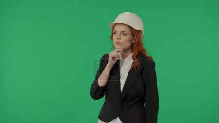 Téléchargez les photos : Une femme architecte réfléchit fort sur un fond d'écran vert dans le studio. Espace publicitaire, maquette d'espace de travail - en image libre de droit