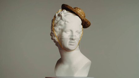 Foto de Primer plano de la antigua estatua de mármol de la diosa Venus en pequeño sombrero de paja. Retrato del busto femenino de la época romana. Aislado sobre fondo gris. Concepto abstracto creativo. - Imagen libre de derechos