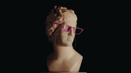 Téléchargez les photos : Gros plan de l'ancienne déesse Vénus statue de marbre en verres roses. Portrait de buste de femme de l'époque romaine sur une plate-forme. Isolé sur fond noir. Concept abstrait créatif. - en image libre de droit