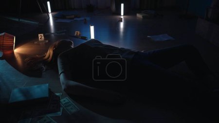 Foto de El cuerpo de una mujer muerta yace en el suelo en un apartamento oscuro. En la escena del crimen, un pogromo, un cuchillo, billetes de dólar marcados como evidencia yacen en el suelo - Imagen libre de derechos