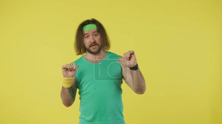 Photo for Man in sportswear pointing at himself, posing at the camera. Portrait of male model in green tank top and headband. Fitness and wellness concept. Isolated on yellow background. - Royalty Free Image