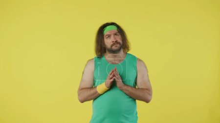 Photo for Man in sportswear depply thinking about something. Portrait of male model in green tank top and headband. Fitness and wellness concept. Isolated on yellow background. - Royalty Free Image
