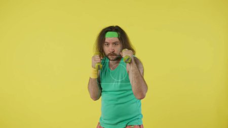 Foto de Hombre en entrenamiento de ropa deportiva con pesas. Retrato de modelo masculino en camiseta verde y diadema. Concepto de fitness y bienestar. Aislado sobre fondo amarillo. - Imagen libre de derechos