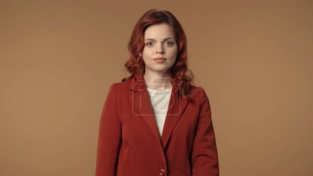 Photo for Medium isolated shot of a serious and calm young business woman standing in front of brown background, looking straight at the camera. Woman looks calm and peaceful. Creative business content. - Royalty Free Image