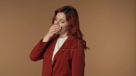 Photo for Medium isolated shot of a young sleepy tired woman yawning, covering her mouth with her hand. Her eyes are half closed. Concept of overworking, late shifts. Business content or advertisement. - Royalty Free Image