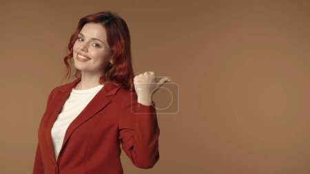 Photo for Medium isolated shot of a satisfied, happy and active young woman pointing her finger, thumb to the right to highlight something behind her. Promotional content, advertising area. Business content. - Royalty Free Image