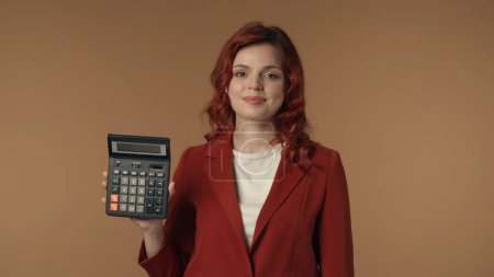 Photo for Medium isolated shot of a joyful and relaxed young woman holding a calculator in her hand. Woman is looking at the camera. Creative content connected with office, accounting and banking. - Royalty Free Image