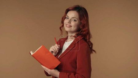 Photo for Medium isolated shot of a satisfied, happy and active young woman holding a pen and a journal, notebook, diary. Woman is smiling at the camera. Business content or advertisement. - Royalty Free Image