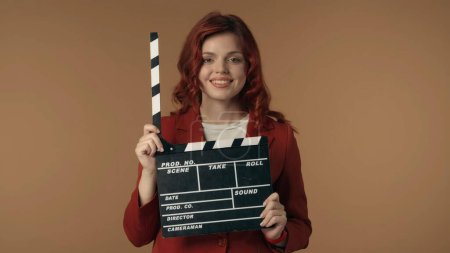Photo for Medium isolated shot satisfied, happy and relaxed young woman holding an opened movie clicker, slate, clapperboard in front of herself. Woman is looking at the camera. Movie, film, cinema. - Royalty Free Image