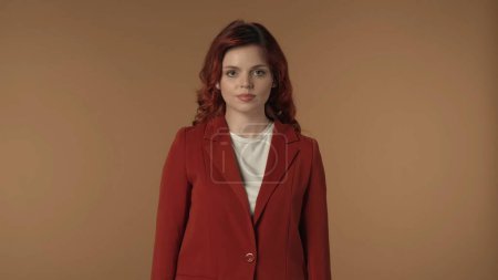 Photo for Medium isolated shot of a serious and calm young business woman standing in front of brown background, looking straight at the camera. Woman looks calm and peaceful. Creative business content. - Royalty Free Image