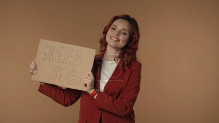 Photo for Medium isolated shot of a joyful and active young woman holding a piece of cardboard that says need job in her hands. Woman is looking from behind it. Job, vacancy offer or advertisement. - Royalty Free Image